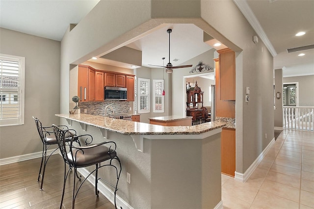 kitchen featuring stainless steel appliances, a kitchen breakfast bar, ceiling fan, kitchen peninsula, and crown molding