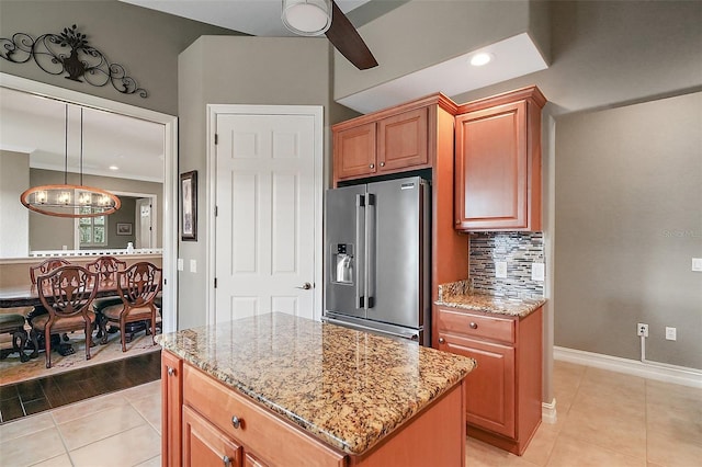 kitchen with a center island, light tile patterned floors, decorative backsplash, light stone countertops, and stainless steel refrigerator with ice dispenser