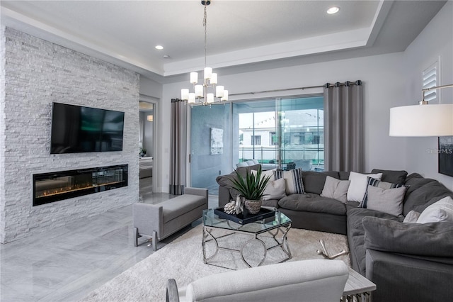 living room with a fireplace, a raised ceiling, and a notable chandelier