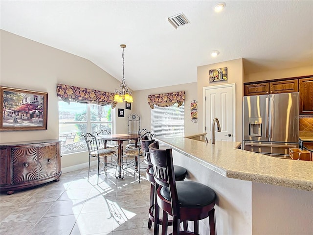 kitchen with vaulted ceiling, decorative light fixtures, stainless steel fridge, a kitchen bar, and light stone counters