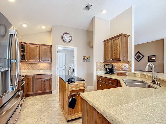 kitchen featuring tasteful backsplash, lofted ceiling, sink, stainless steel fridge with ice dispenser, and washing machine and dryer
