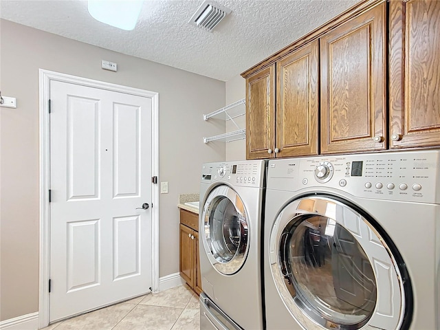 clothes washing area featuring light tile patterned flooring, cabinets, washing machine and dryer, and a textured ceiling