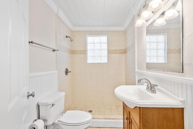 bathroom with toilet, vanity, ornamental molding, and a tile shower