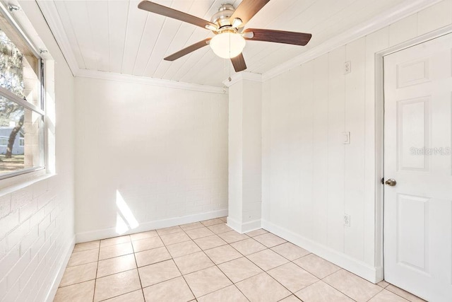 spare room featuring ceiling fan, brick wall, light tile patterned floors, and ornamental molding