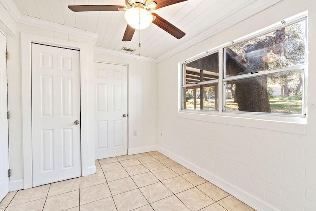 unfurnished bedroom featuring ceiling fan, brick wall, ornamental molding, and light tile patterned flooring