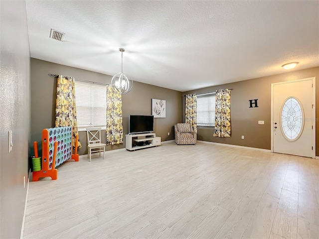 interior space with an inviting chandelier, a textured ceiling, and light wood-type flooring