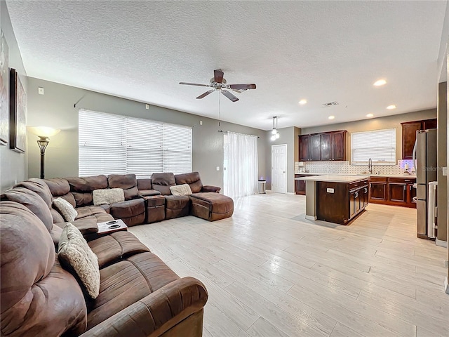 living room featuring ceiling fan, sink, light hardwood / wood-style flooring, and a textured ceiling