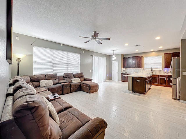 living room featuring ceiling fan, a wealth of natural light, a textured ceiling, and light wood-type flooring