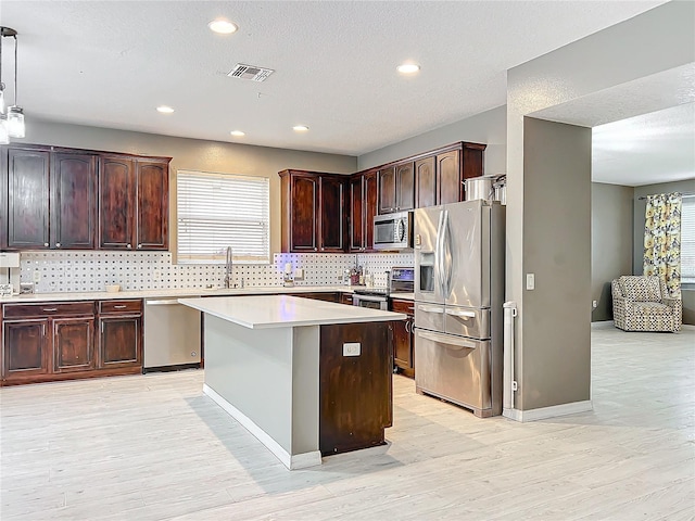 kitchen featuring appliances with stainless steel finishes, decorative light fixtures, sink, decorative backsplash, and a center island