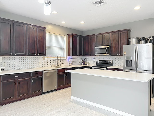 kitchen featuring a kitchen island, sink, dark brown cabinetry, stainless steel appliances, and light hardwood / wood-style flooring