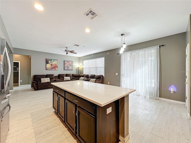 kitchen with dark brown cabinetry, decorative light fixtures, a center island, light hardwood / wood-style flooring, and a textured ceiling