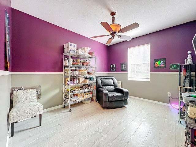 living area featuring hardwood / wood-style flooring, ceiling fan, and a textured ceiling