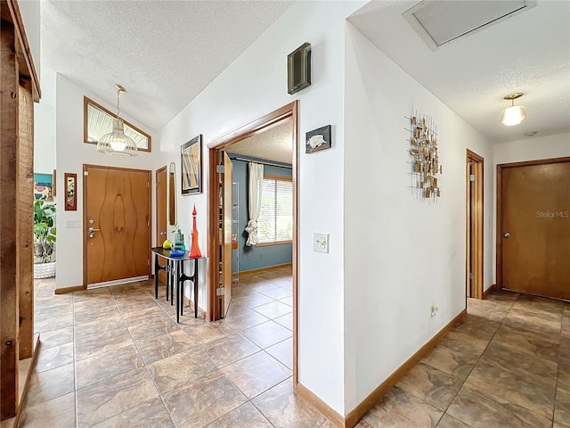 foyer featuring a textured ceiling, vaulted ceiling, visible vents, and baseboards