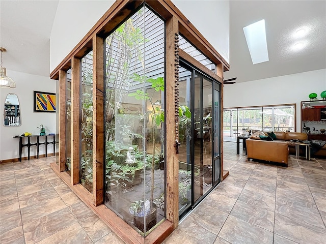 interior space featuring high vaulted ceiling, a skylight, and baseboards