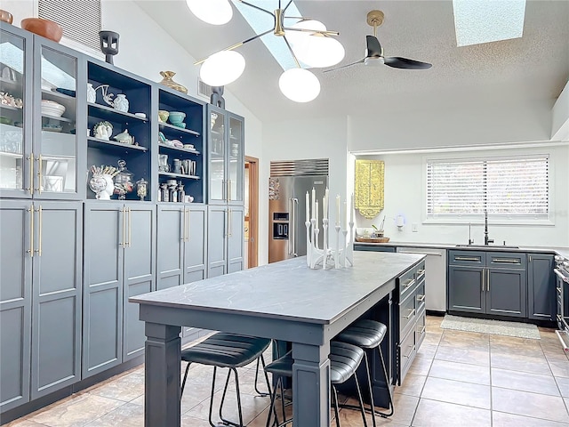 kitchen with a sink, appliances with stainless steel finishes, a center island, open shelves, and glass insert cabinets