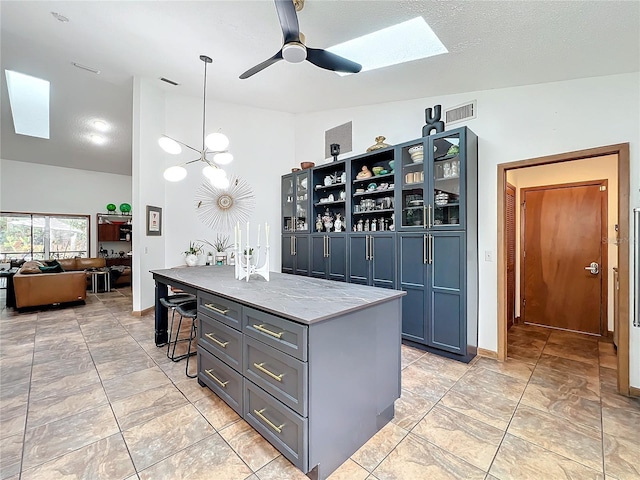 kitchen with visible vents, a kitchen breakfast bar, an island with sink, glass insert cabinets, and pendant lighting