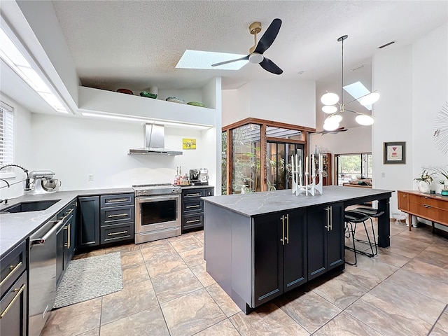 kitchen with wall chimney exhaust hood, appliances with stainless steel finishes, decorative light fixtures, a center island, and a sink