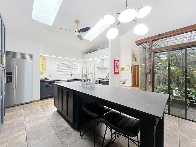 kitchen with stainless steel built in fridge, a sink, a center island, lofted ceiling with skylight, and decorative light fixtures