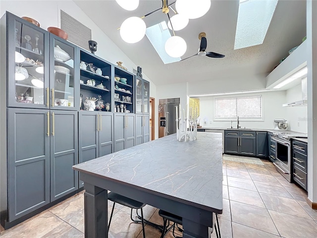 kitchen featuring light stone counters, premium appliances, a sink, vaulted ceiling, and glass insert cabinets