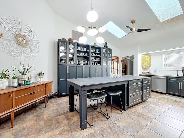 kitchen featuring stainless steel appliances, hanging light fixtures, lofted ceiling with skylight, glass insert cabinets, and a sink