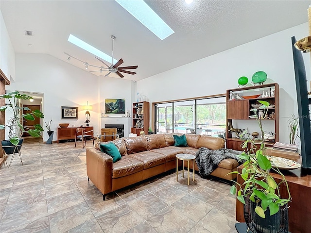 living room featuring a skylight, a fireplace, visible vents, and high vaulted ceiling