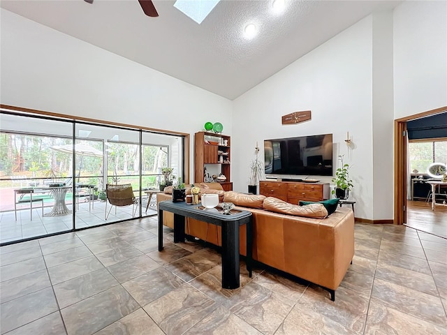 living area with ceiling fan, high vaulted ceiling, plenty of natural light, and a skylight