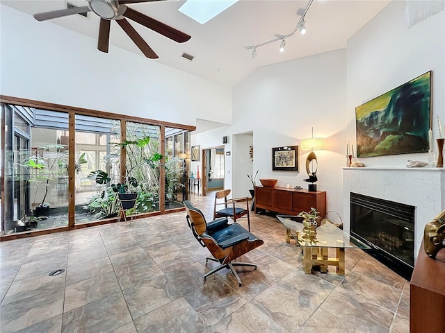 interior space with a skylight, visible vents, a tile fireplace, ceiling fan, and high vaulted ceiling