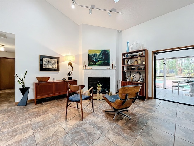 sitting room with baseboards, high vaulted ceiling, a tiled fireplace, and track lighting