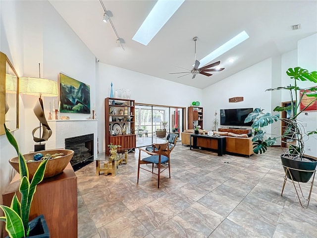 living room featuring a skylight, visible vents, a ceiling fan, a glass covered fireplace, and high vaulted ceiling