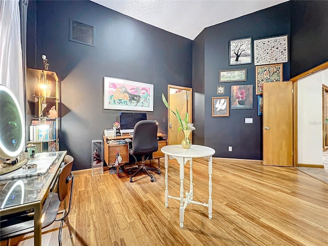 office space with lofted ceiling, baseboards, visible vents, and wood finished floors