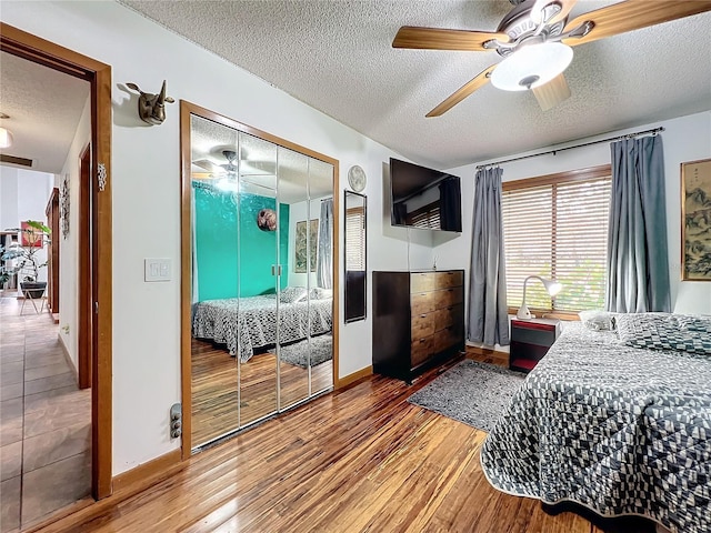 bedroom with a textured ceiling, ceiling fan, wood finished floors, baseboards, and a closet