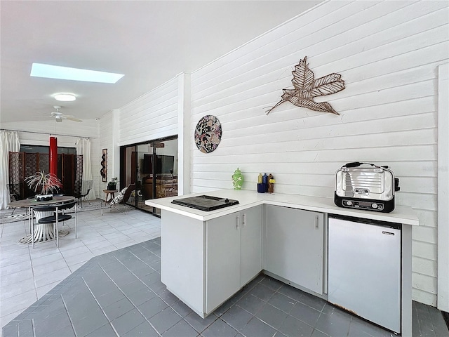 kitchen with a skylight, light countertops, freestanding refrigerator, a peninsula, and dark tile patterned floors