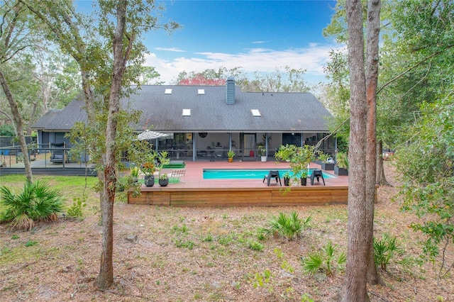 back of house with a shingled roof, fence, an outdoor pool, and a wooden deck