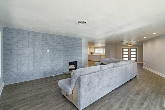 living room featuring a fireplace, french doors, dark wood-type flooring, and brick wall