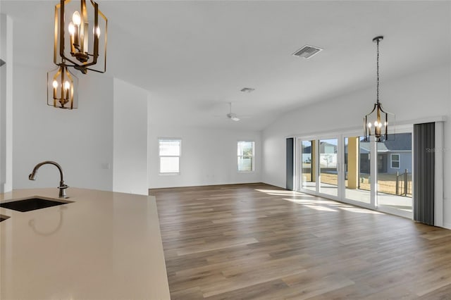 unfurnished living room featuring lofted ceiling, sink, ceiling fan with notable chandelier, and hardwood / wood-style floors