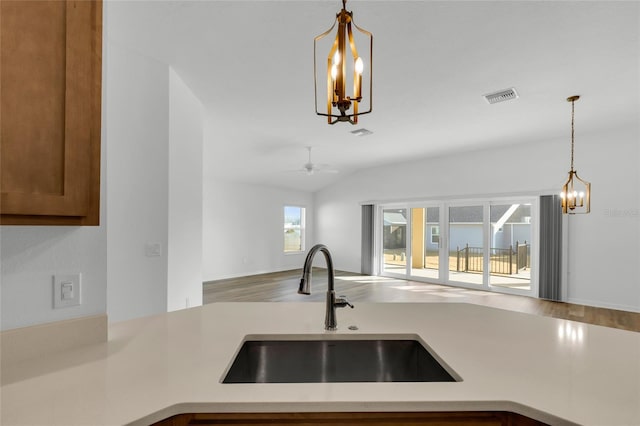 kitchen featuring vaulted ceiling, hardwood / wood-style floors, ceiling fan with notable chandelier, pendant lighting, and sink