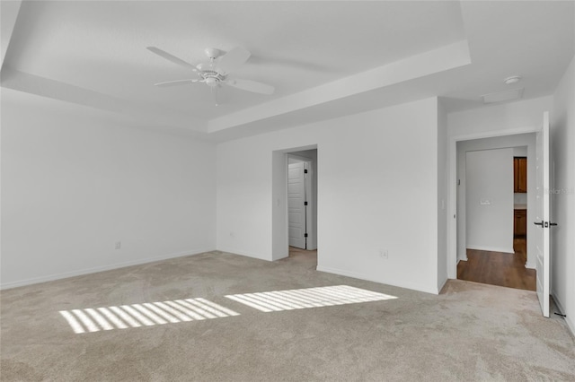 spare room featuring a tray ceiling, light colored carpet, and ceiling fan