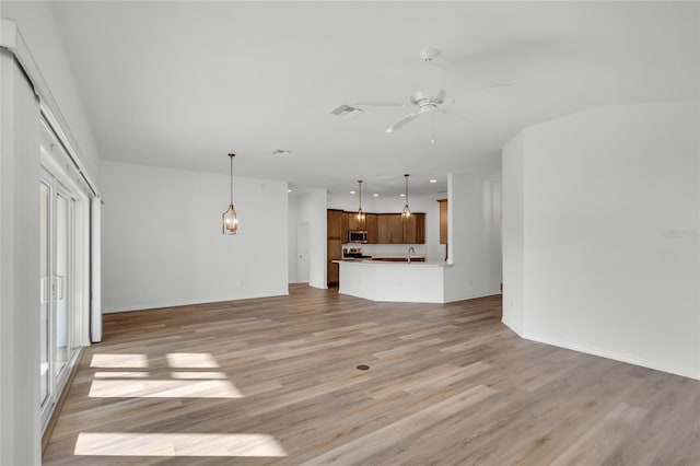 unfurnished living room with sink, ceiling fan with notable chandelier, and light wood-type flooring