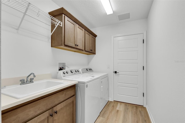 clothes washing area with sink, light wood-type flooring, cabinets, washing machine and dryer, and a textured ceiling