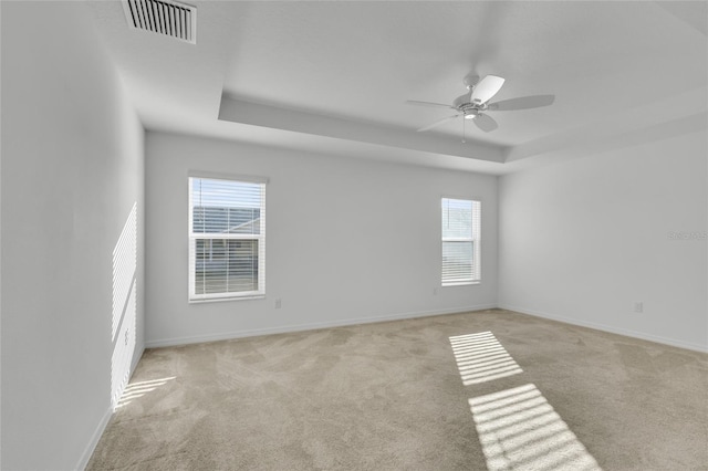 carpeted spare room featuring a raised ceiling and ceiling fan