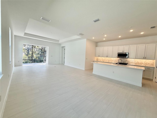 kitchen featuring white cabinetry, sink, tasteful backsplash, an island with sink, and a tray ceiling