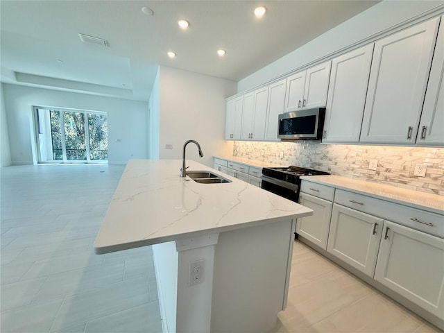 kitchen with black gas range, light stone countertops, sink, a kitchen island with sink, and decorative backsplash