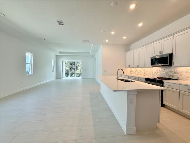 kitchen featuring white cabinets, sink, decorative backsplash, an island with sink, and light stone counters