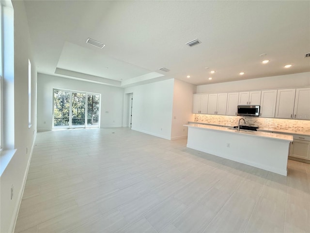 kitchen featuring white cabinets, sink, backsplash, and an island with sink