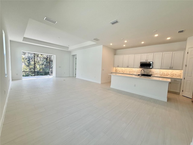 kitchen featuring backsplash, a center island with sink, white cabinets, and sink