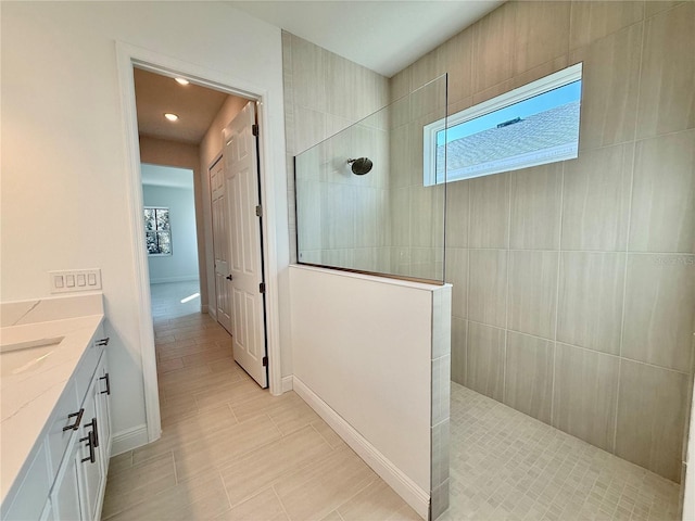 bathroom featuring a tile shower, vanity, and a healthy amount of sunlight