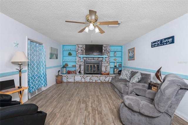 living room with built in shelves, a textured ceiling, hardwood / wood-style flooring, and a stone fireplace