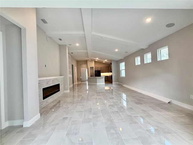 unfurnished living room with a stone fireplace and lofted ceiling with beams