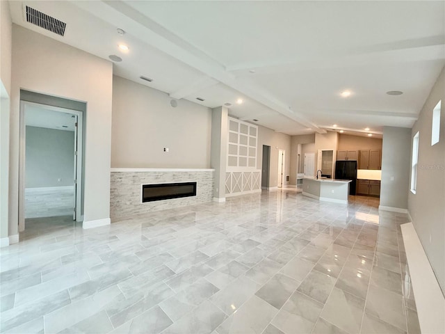 unfurnished living room featuring vaulted ceiling with beams, a stone fireplace, and sink