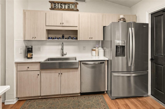 kitchen with appliances with stainless steel finishes, sink, backsplash, and light hardwood / wood-style flooring